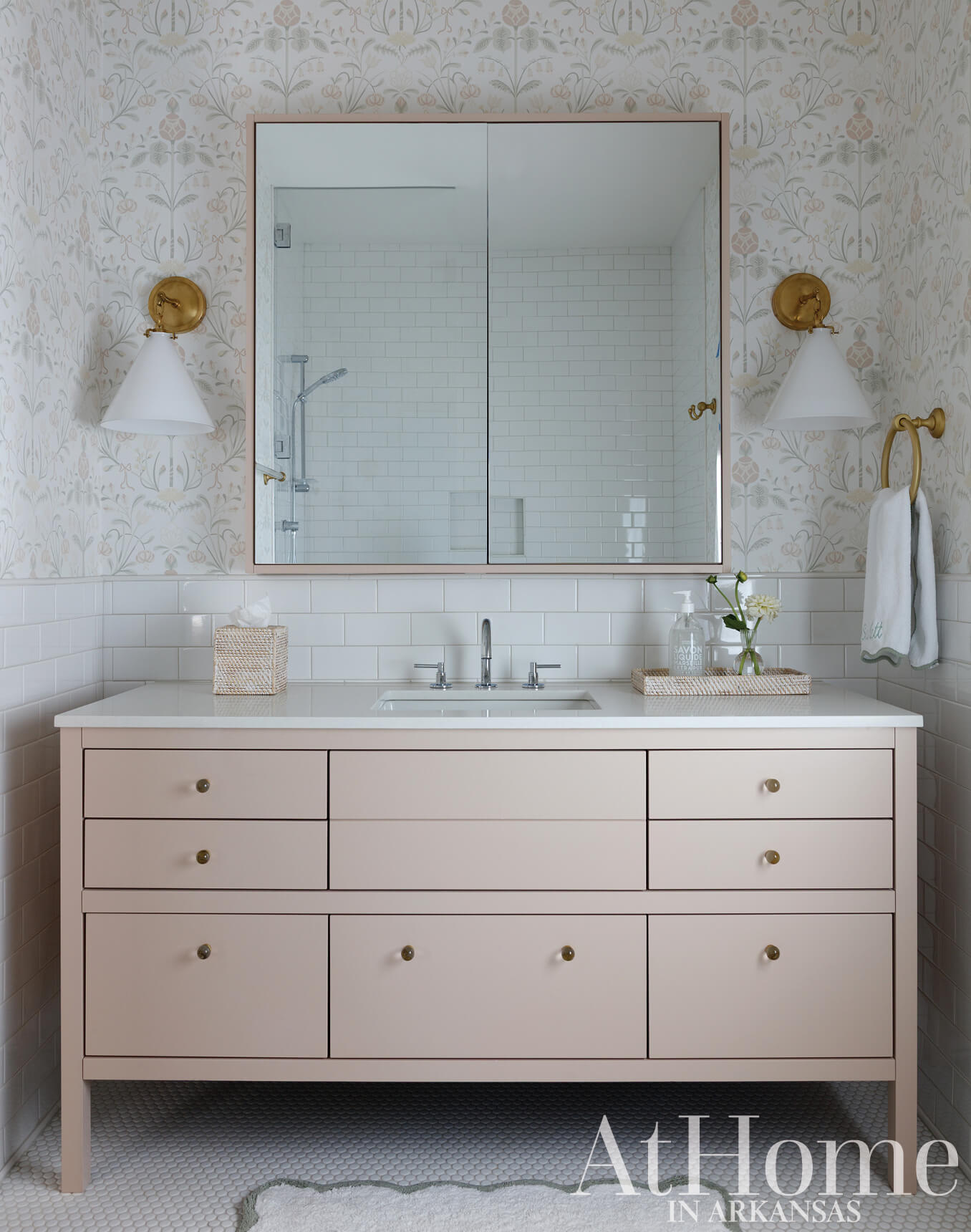 Pink vanity with mirror, sconces, and tile backsplash.
