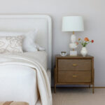 White bed with textured blanket and lamp on nightstand.