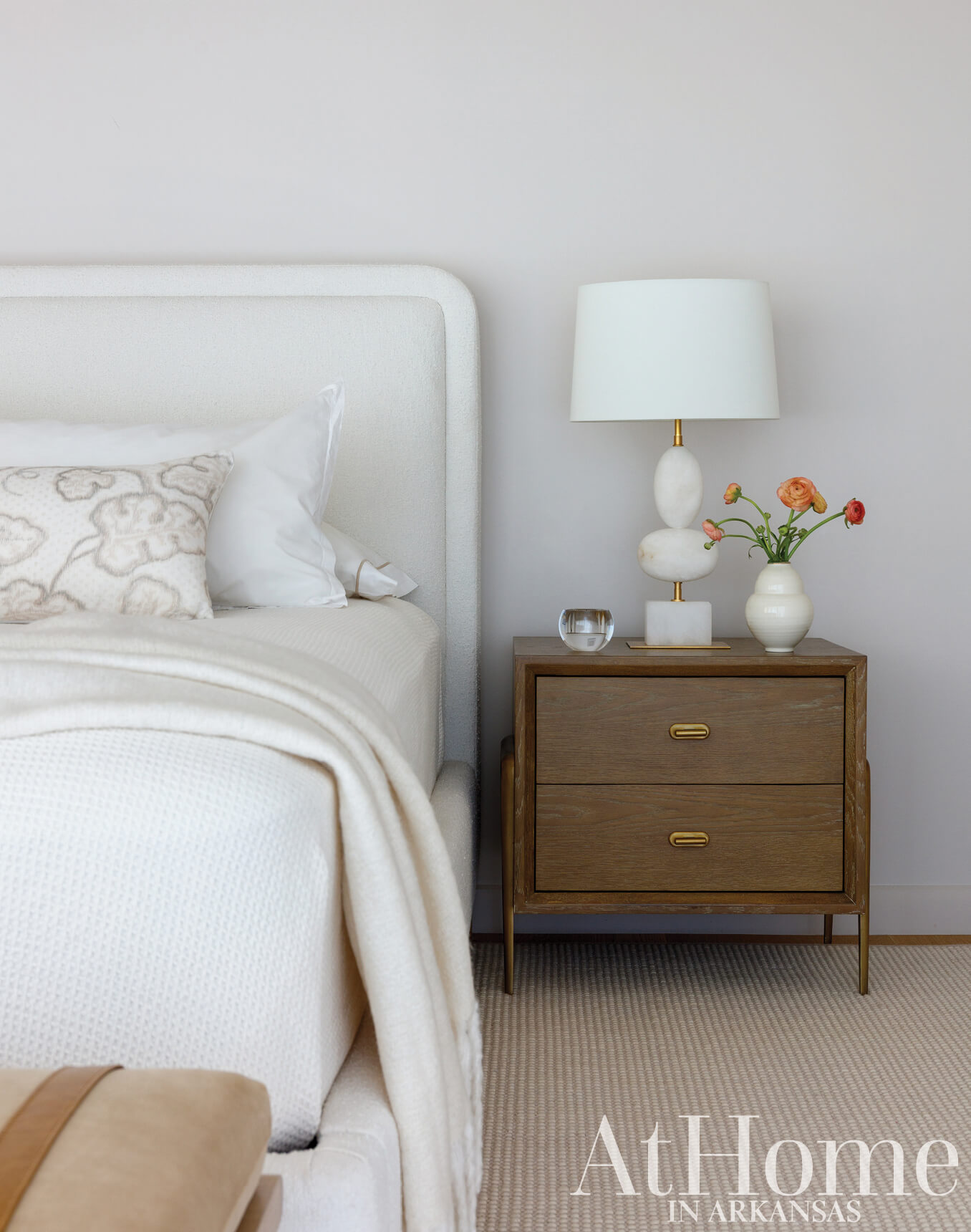 White bed with textured blanket and lamp on nightstand.
