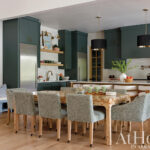 Dark green kitchen island with a stainless steel refrigerator and wooden dining table.