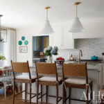 White kitchen with brass pendant lights and blue cabinetry.