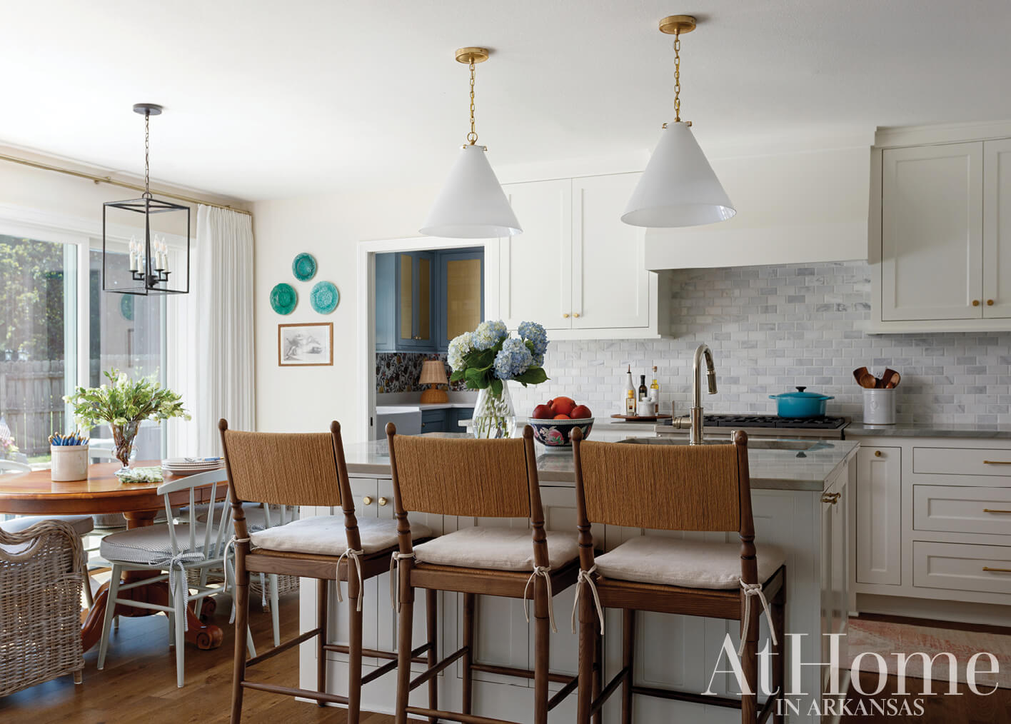 White kitchen with brass pendant lights and blue cabinetry.