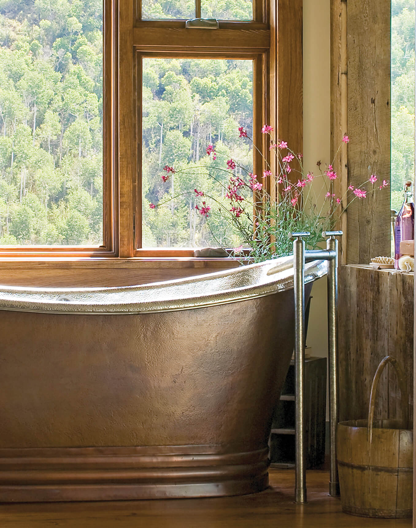 Copper bathtub with wooden surround and floral arrangement.