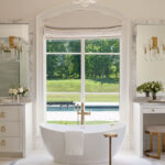 Marble bathroom with large windows overlooking a pool and landscape.