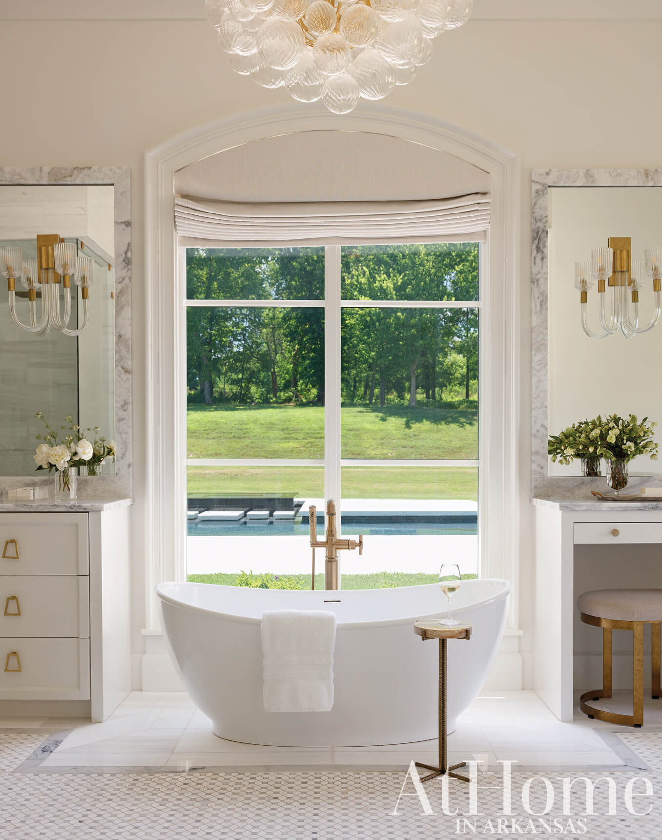 Marble bathroom with large windows overlooking a pool and landscape.