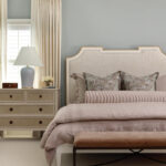 Master bedroom with a beige upholstered bed, pale blue walls, and a dresser.