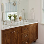 Wooden vanity with silver fixtures and mirror, window, and decorative accents.