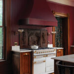 Dark wood cabinetry, maroon walls, and a large range hood.
