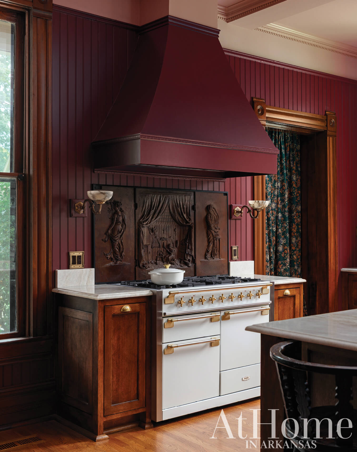 Dark wood cabinetry, maroon walls, and a large range hood.