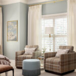 Cream-colored armchairs with plaid cushions and a teal ottoman in a bedroom.