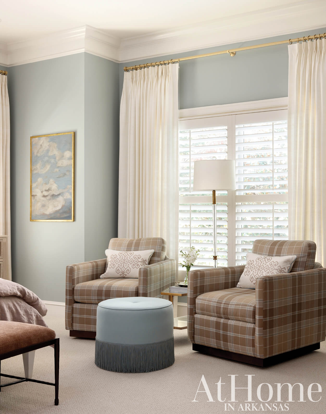 Cream-colored armchairs with plaid cushions and a teal ottoman in a bedroom.