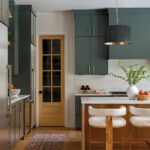 Dark green kitchen cabinets with a white marble countertop and wood island.