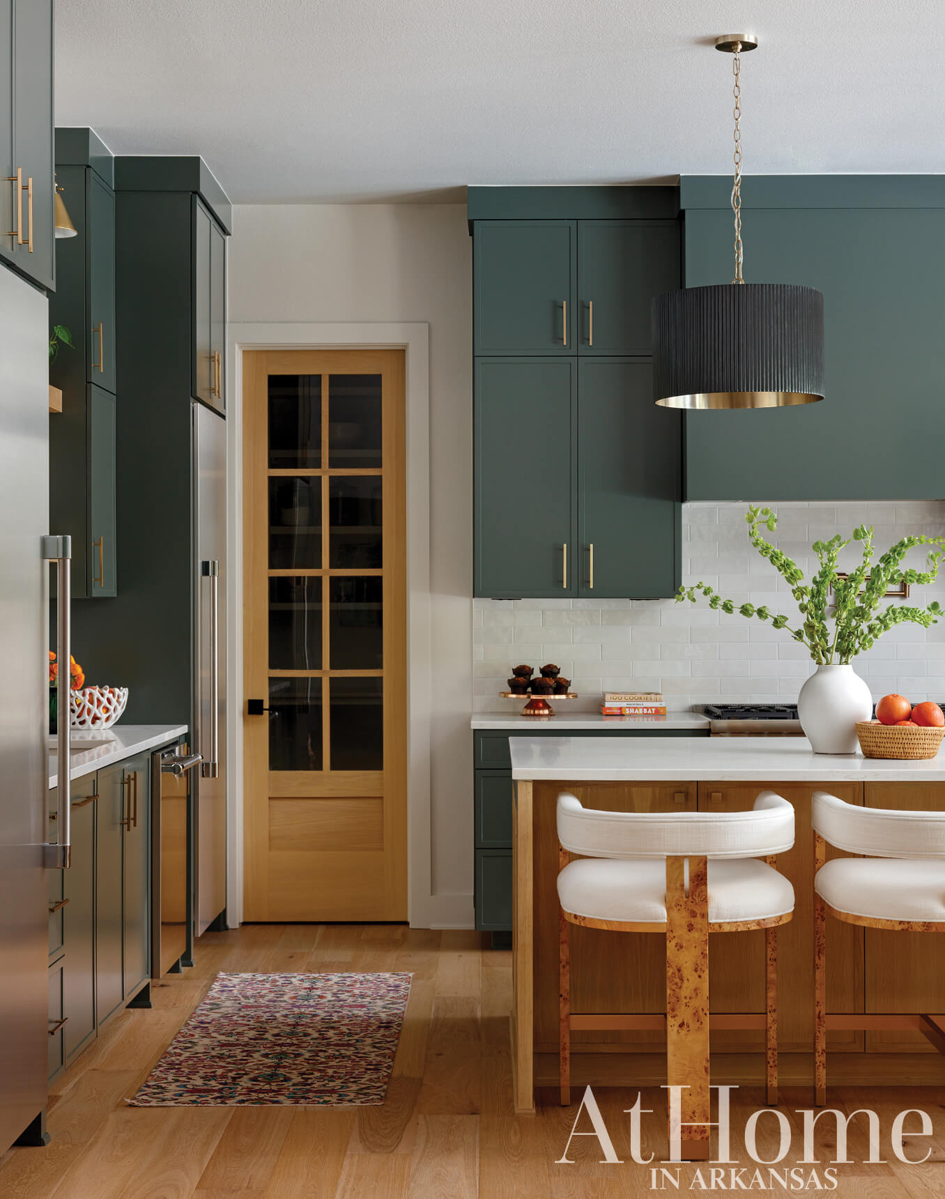 Dark green kitchen cabinets with a white marble countertop and wood island.