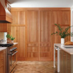 Wooden cabinetry, range hood, and herringbone flooring in a kitchen.