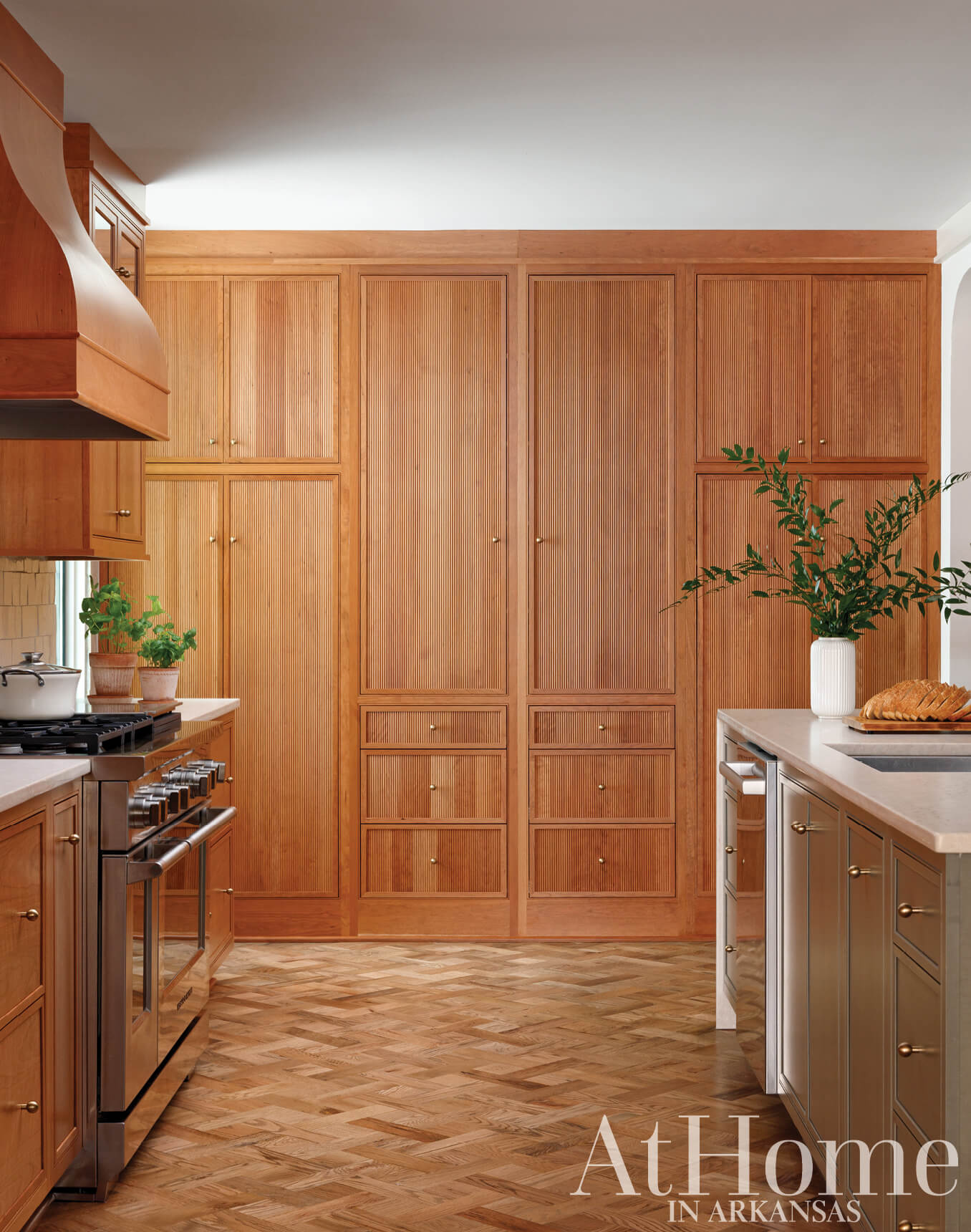Wooden cabinetry, range hood, and herringbone flooring in a kitchen.