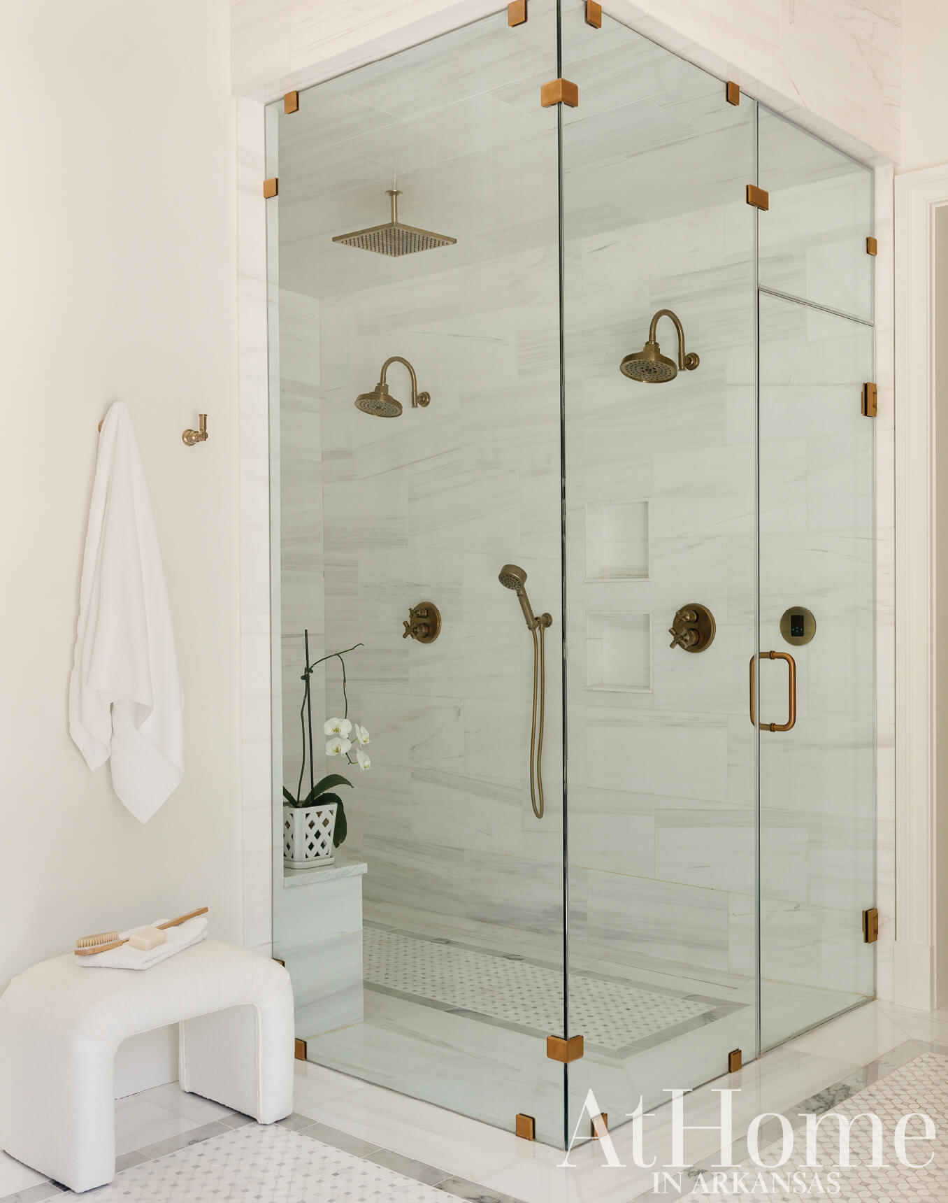 White marble shower with brass fixtures and glass enclosure.