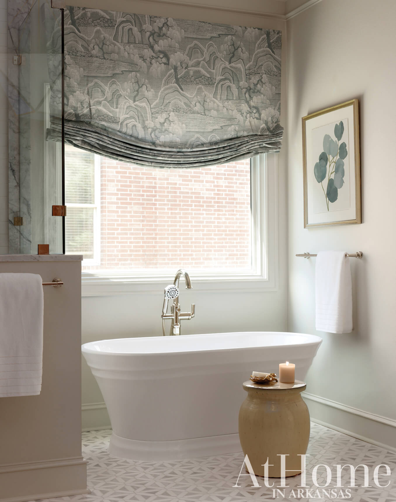 Gray patterned roman shade, marble bathtub, and brick wall in bathroom.