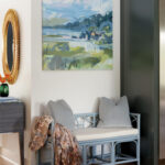 Gray bench with woven seat and cushions, artwork, and decorative mirror.