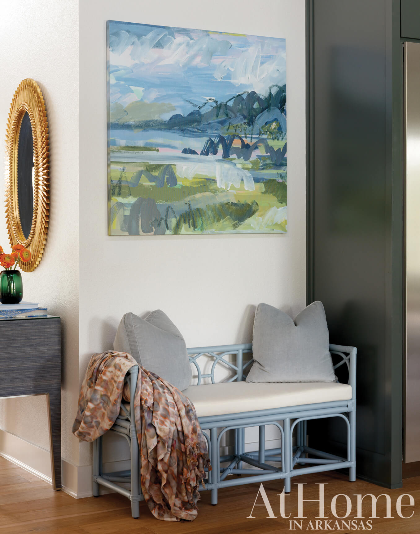 Gray bench with woven seat and cushions, artwork, and decorative mirror.