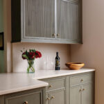 Gray and green cabinetry with brass hardware, wine, and flowers.