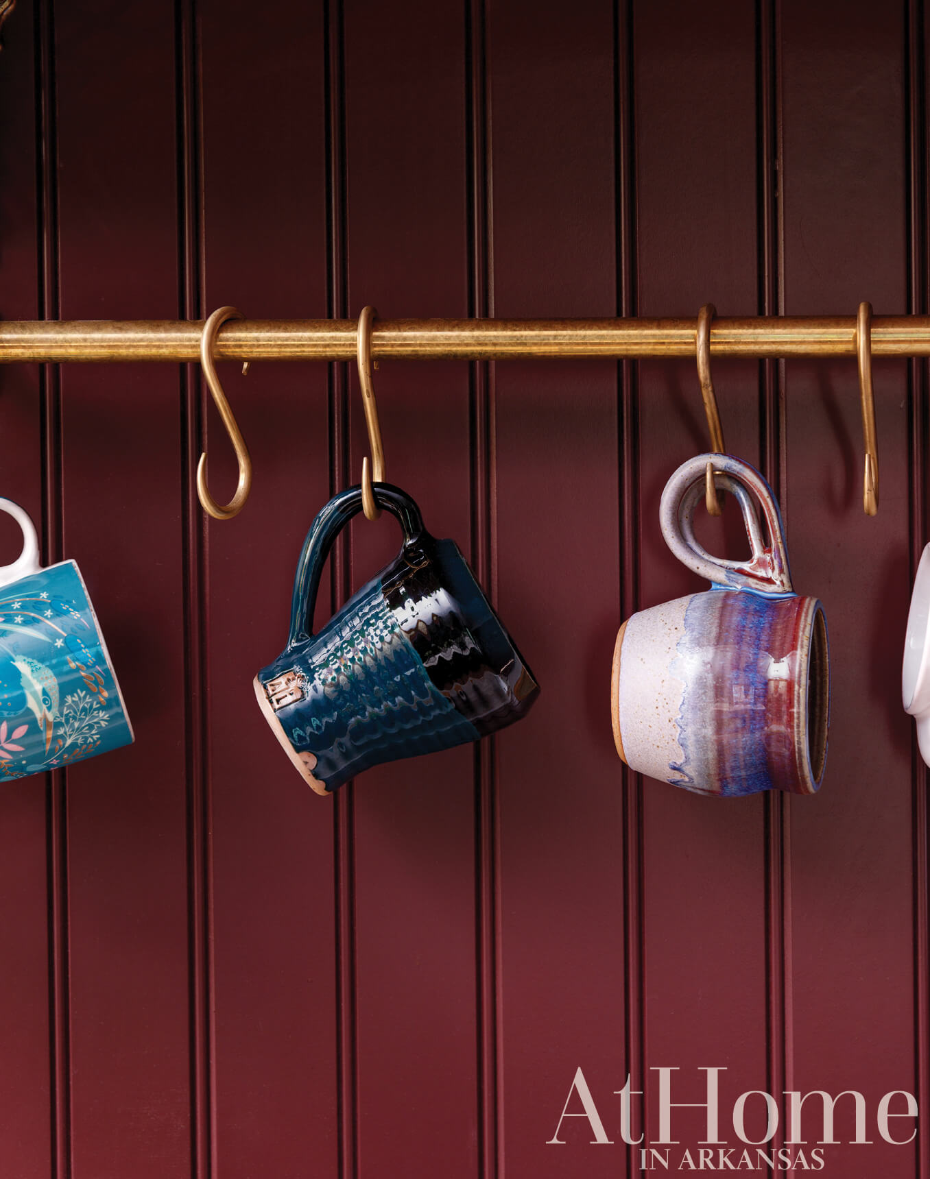 Dark red paneled wall with gold mugs and hooks.