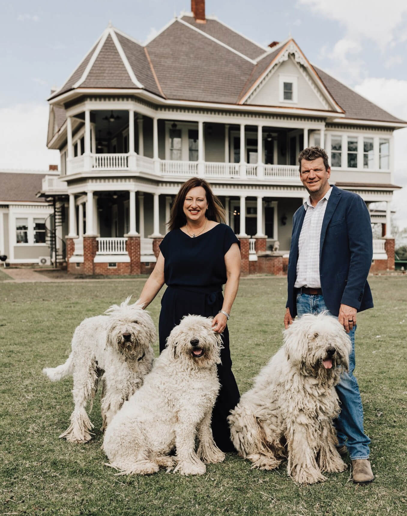 Couple and three dogs stand in front of a Victorian house.