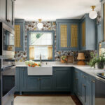 Blue kitchen cabinets with patterned wallpaper and brass fixtures.