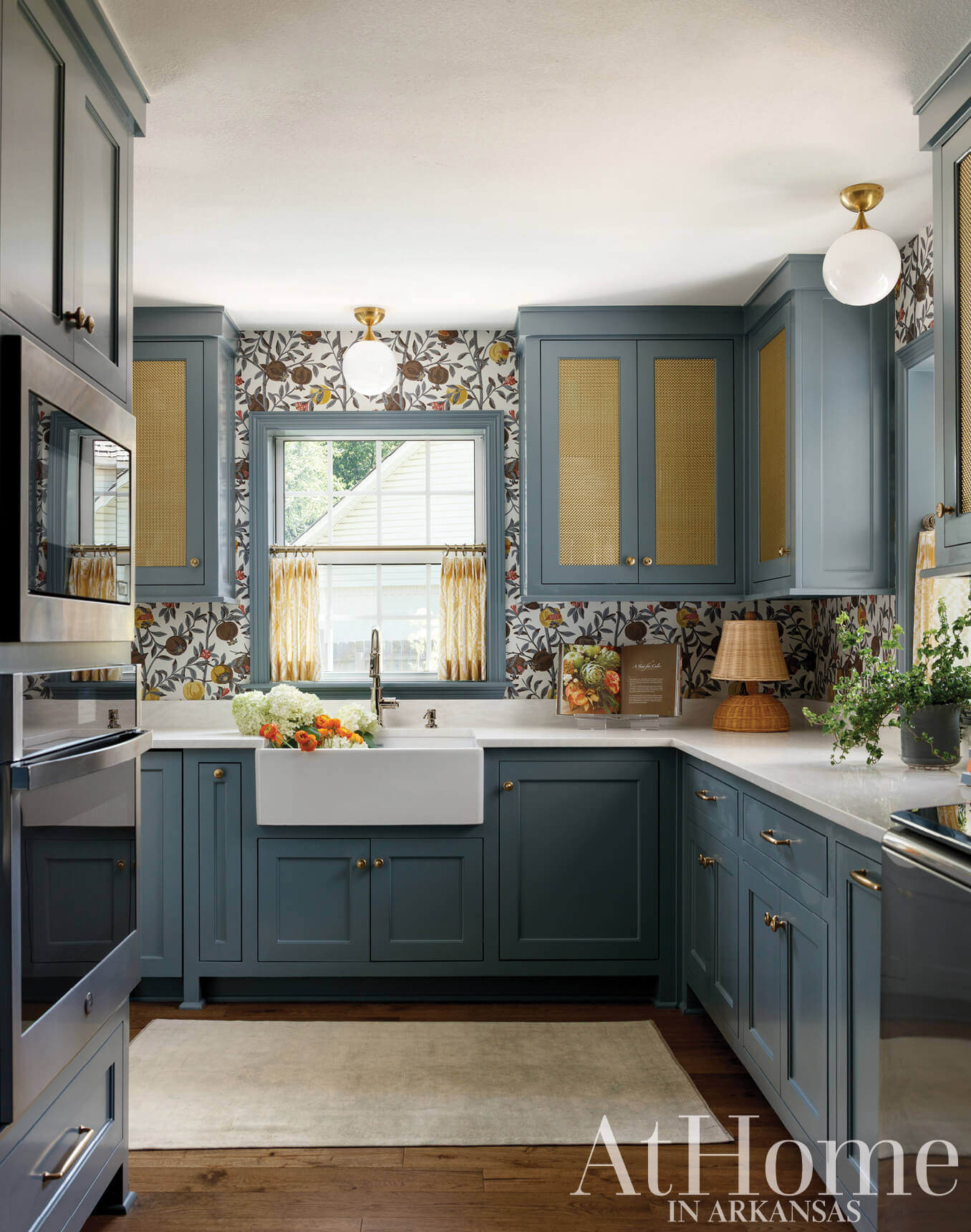 Blue kitchen cabinets with patterned wallpaper and brass fixtures.