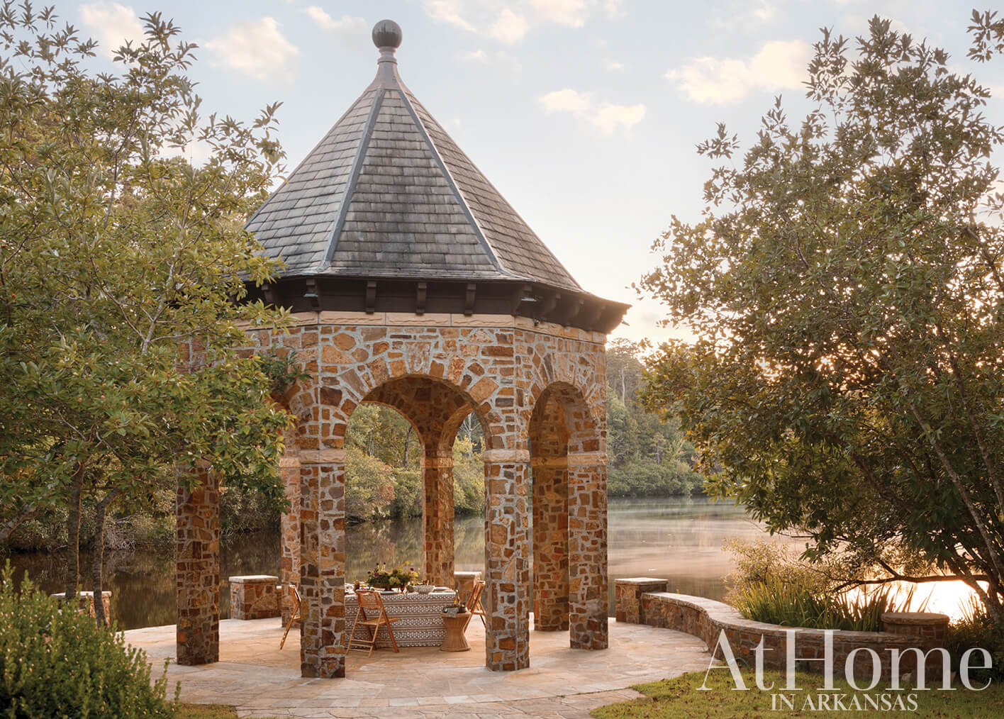 Stone gazebo with a slate roof, overlooking a lake.