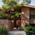 Brick mid-century modern home with landscaping and a tree.