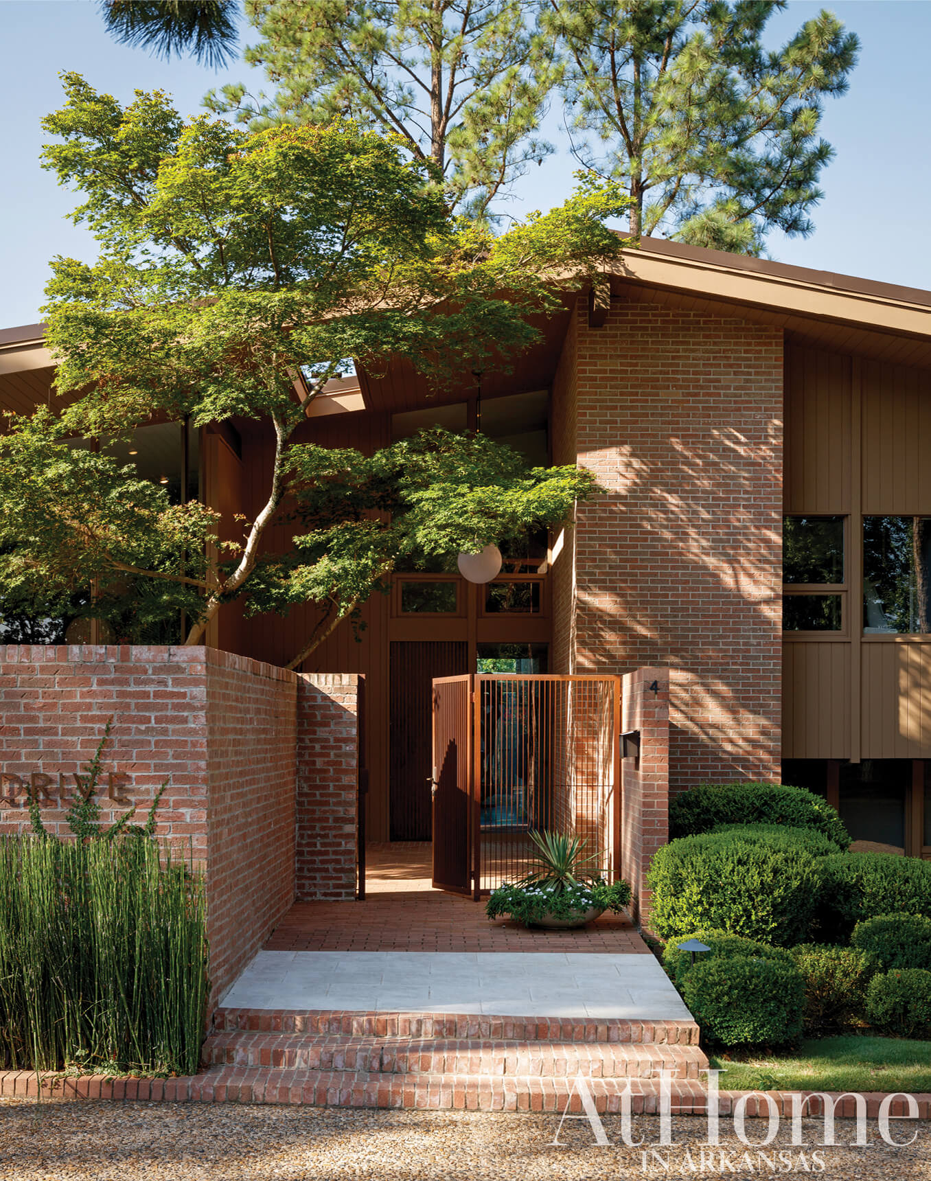 Brick mid-century modern home with landscaping and a tree.