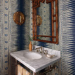 Blue and white patterned wall with bamboo mirror and marble sink.