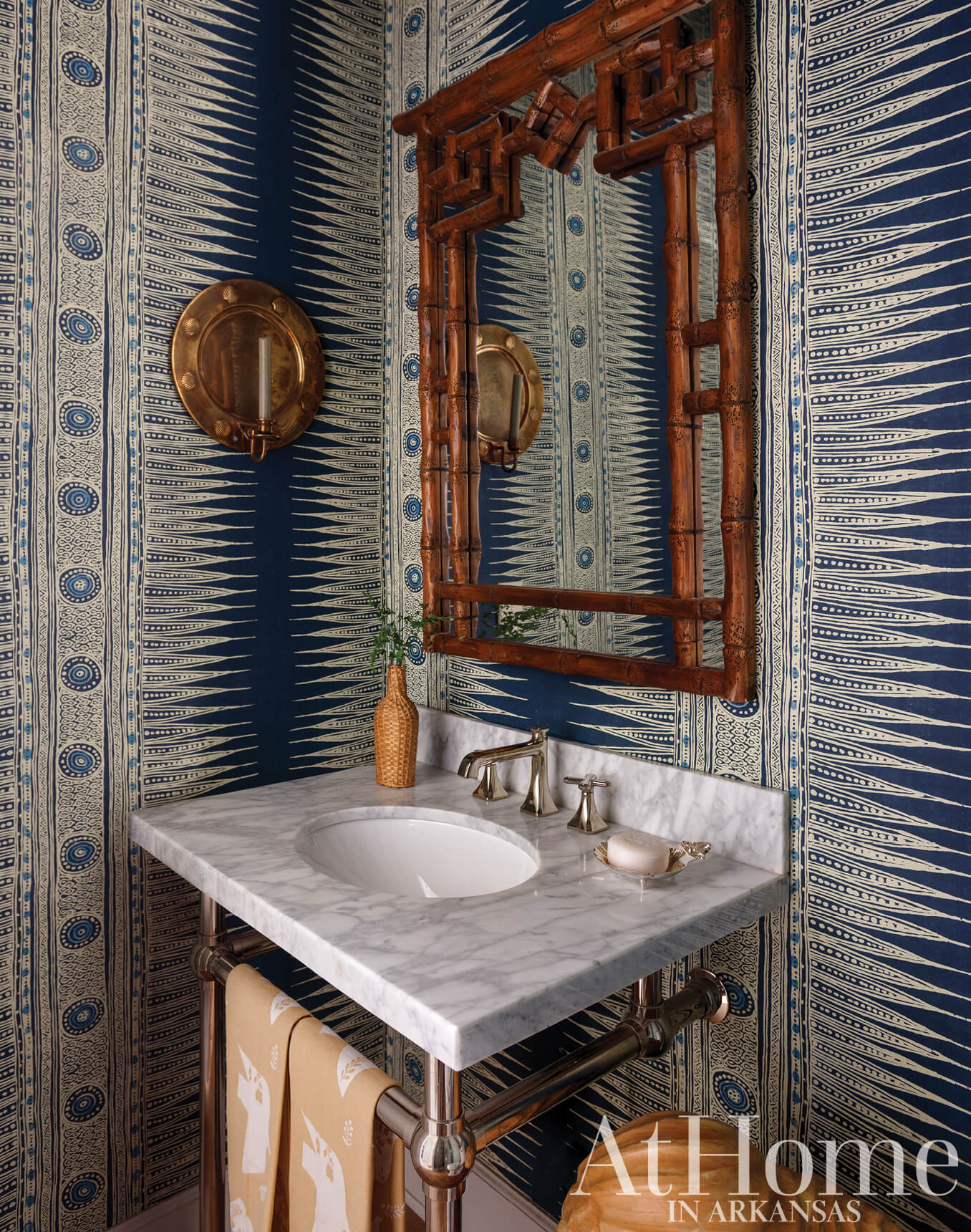 Blue and white patterned wall with bamboo mirror and marble sink.