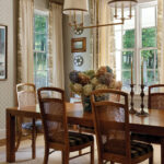 Dining room with patterned wallpaper, wooden table, and gold chandelier.