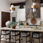 Kitchen island with marble countertop, black and white bar stools, and brass pendant lights.