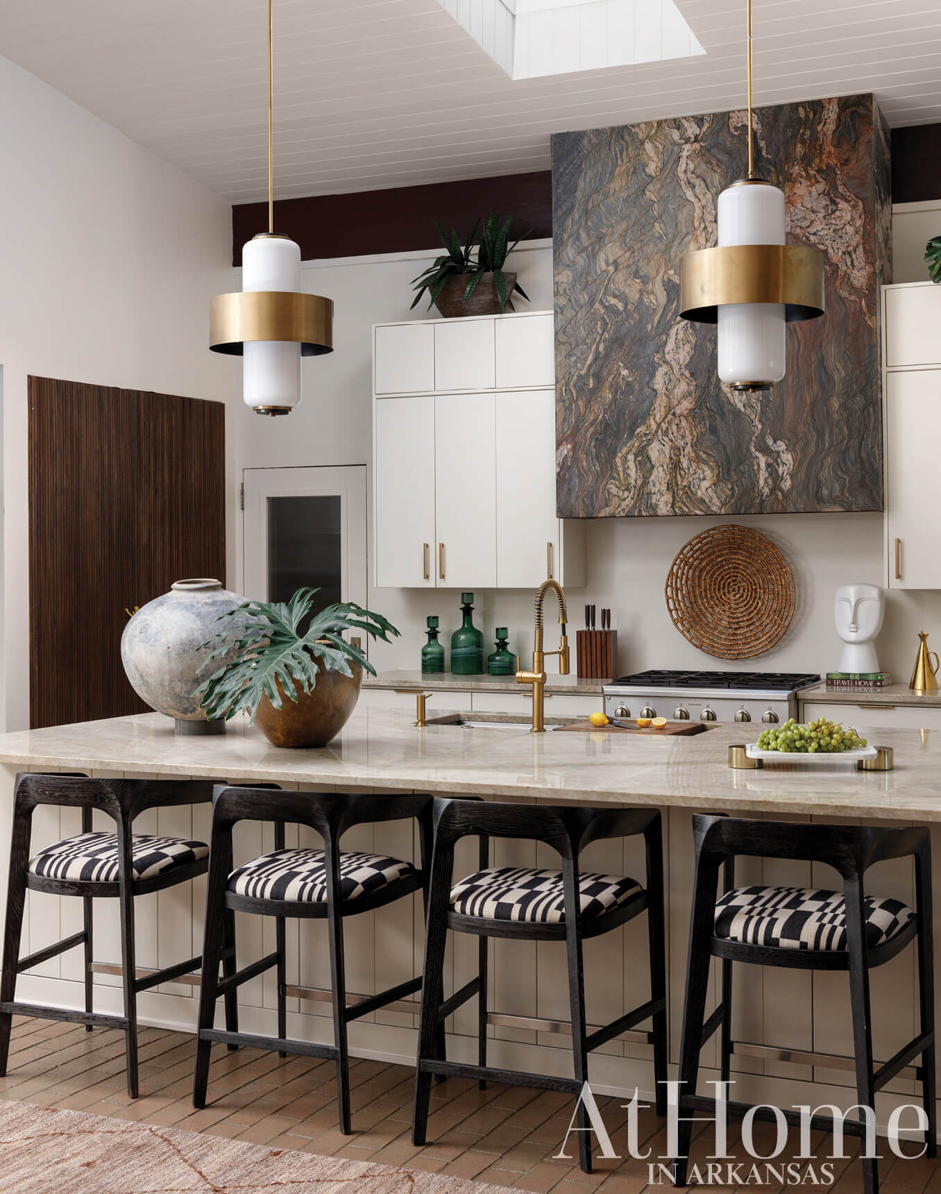 Kitchen island with marble countertop, black and white bar stools, and brass pendant lights.