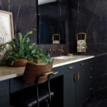 Dark marble wall, gold mirror, and vanity in a bathroom.