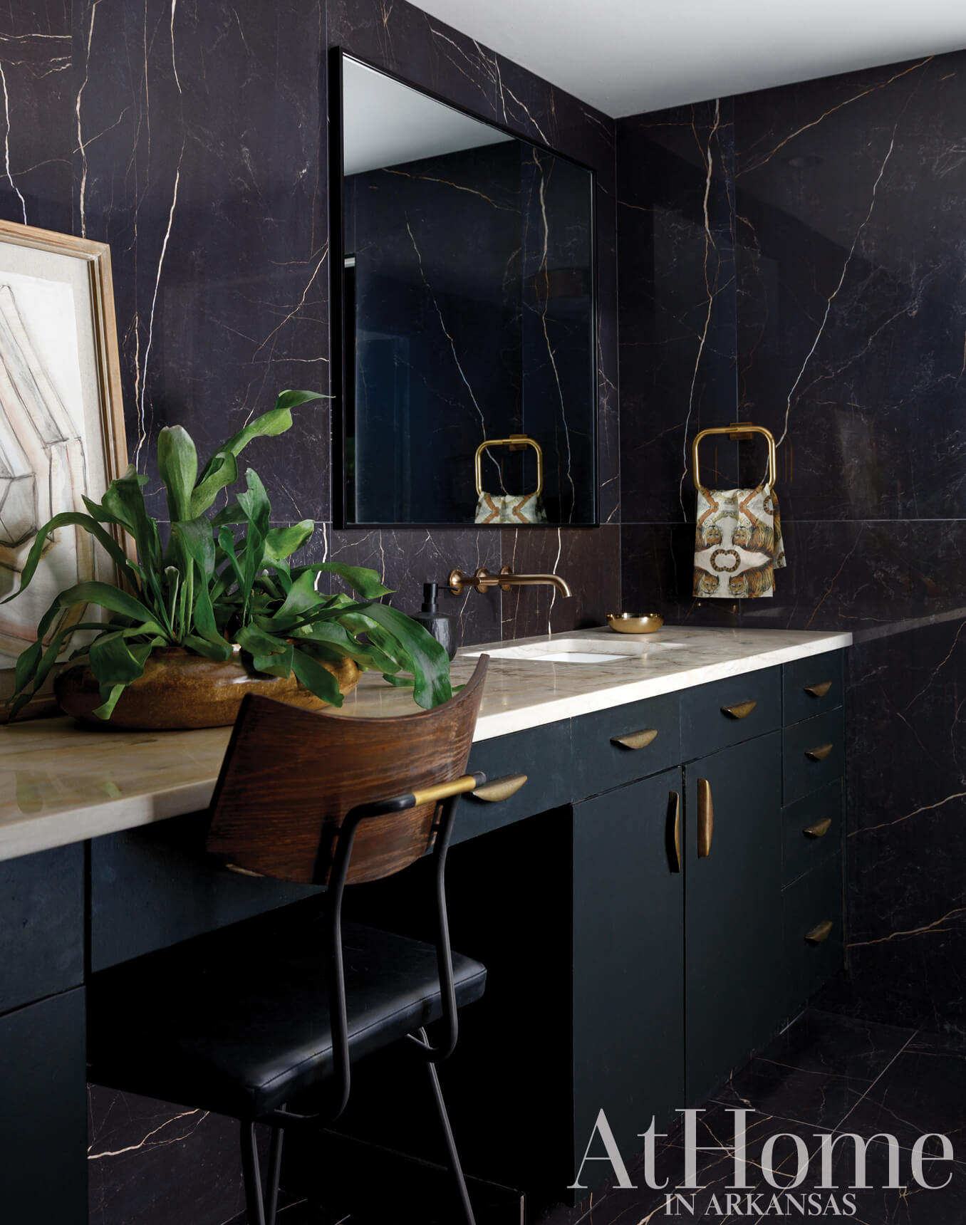Dark marble wall, gold mirror, and vanity in a bathroom.