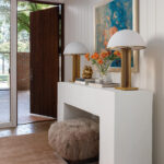 White console table with lamps, books, and a faux fur ottoman.