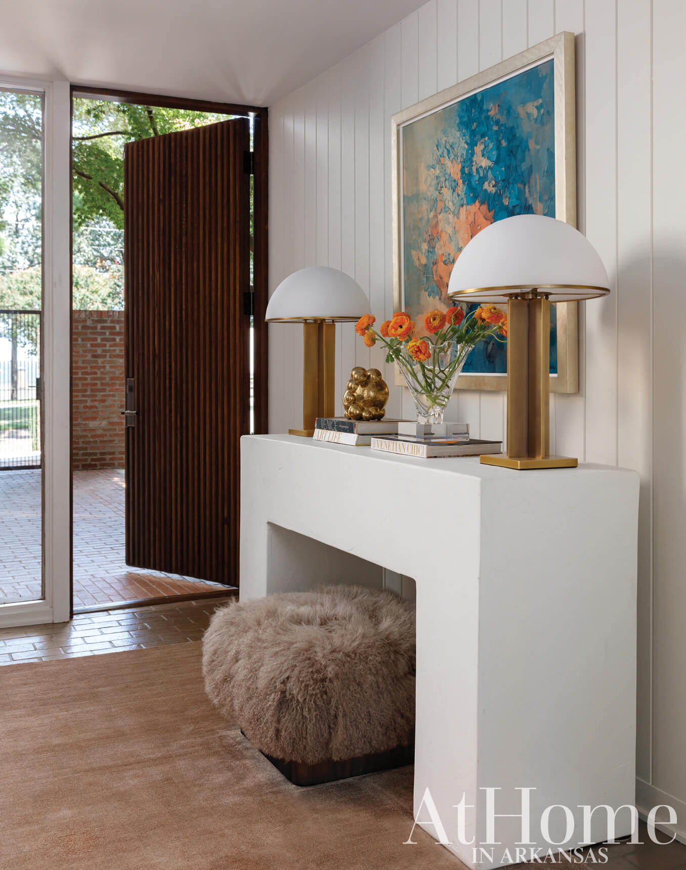 White console table with lamps, books, and a faux fur ottoman.
