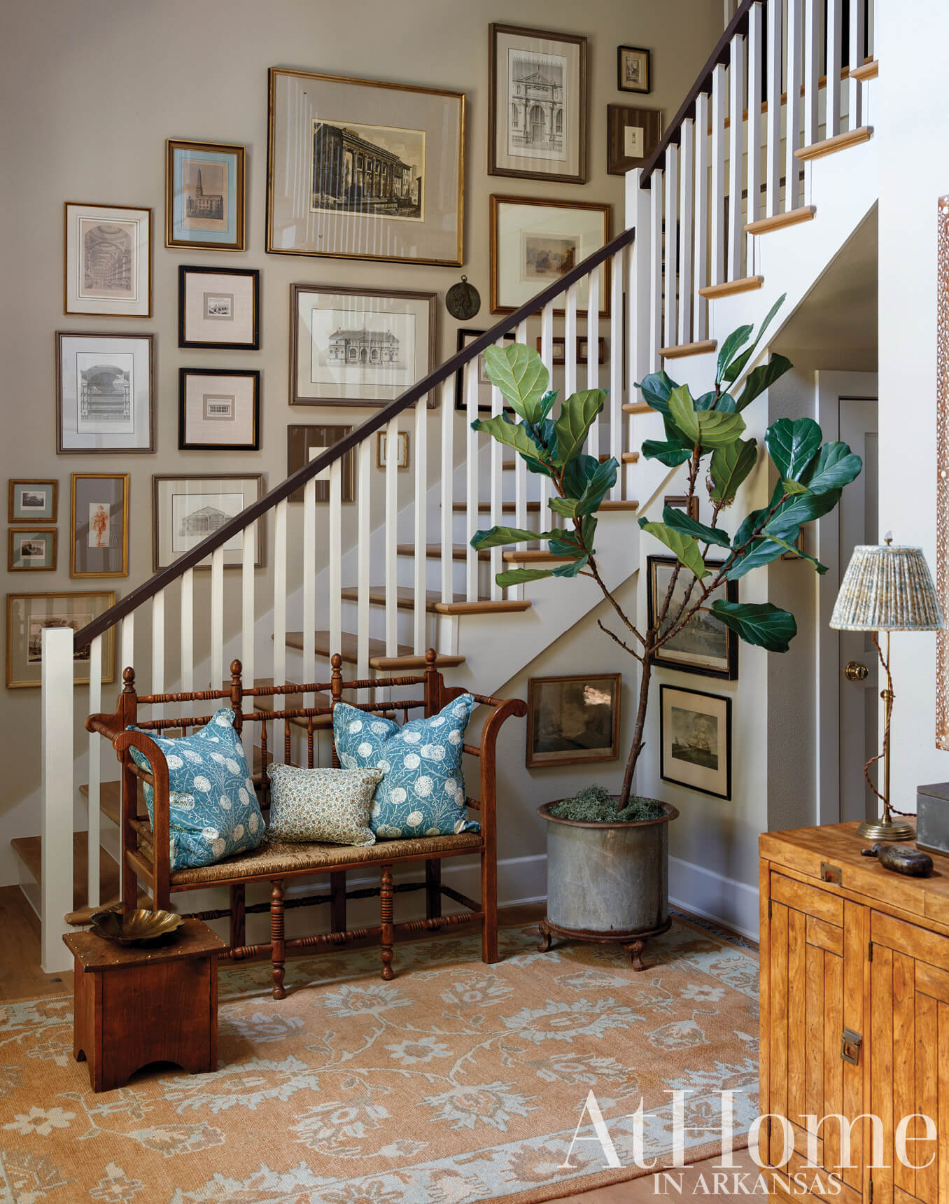 Wooden bench with blue pillows, artwork, and a fiddle-leaf fig plant.