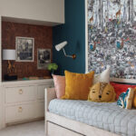 Blue wallpaper with forest print, cork wall, bed with pillows.