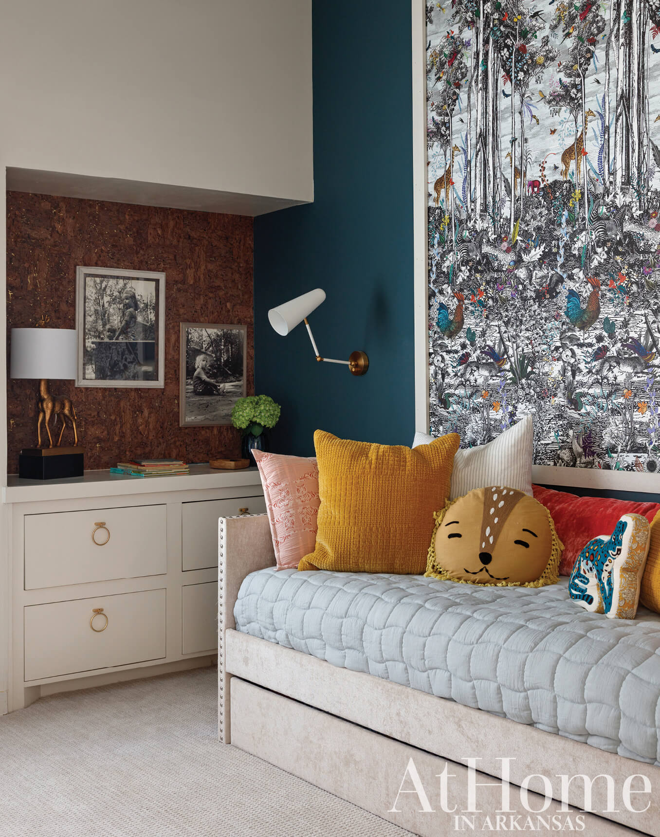 Blue wallpaper with forest print, cork wall, bed with pillows.
